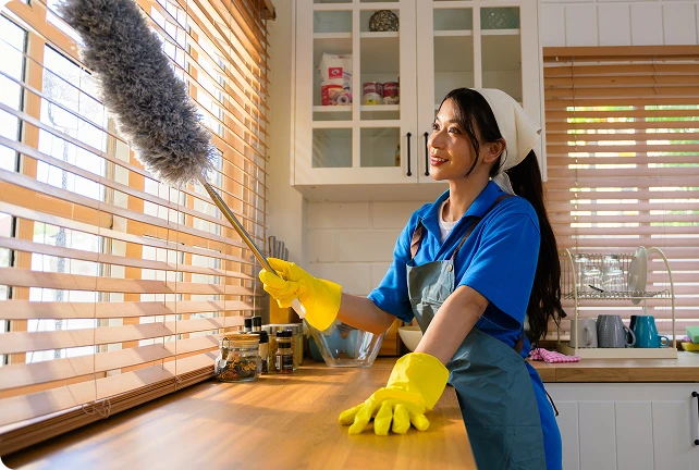 Addetto alle pulizie che spolvera le tende veneziane in una cucina moderna e luminosa usando un piumino in microfibra estensibile.