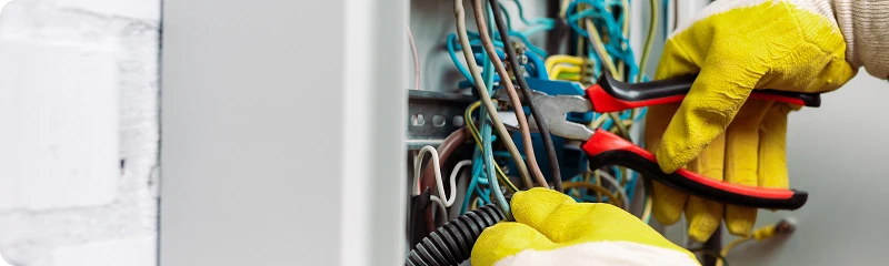 Tecnico che ispeziona e stringe le connessioni elettriche all'interno di un quadro fusibili con un cacciavite.