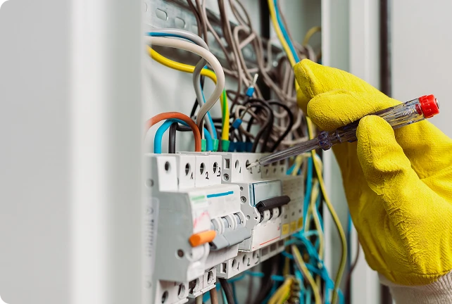 Elettricista che ripara i cavi elettrici all'interno di un quadro di distribuzione usando pinze isolate.