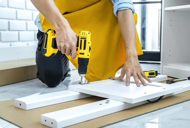 Professionista che monta un armadio bianco usando un trapano a batteria durante l'installazione domestica.